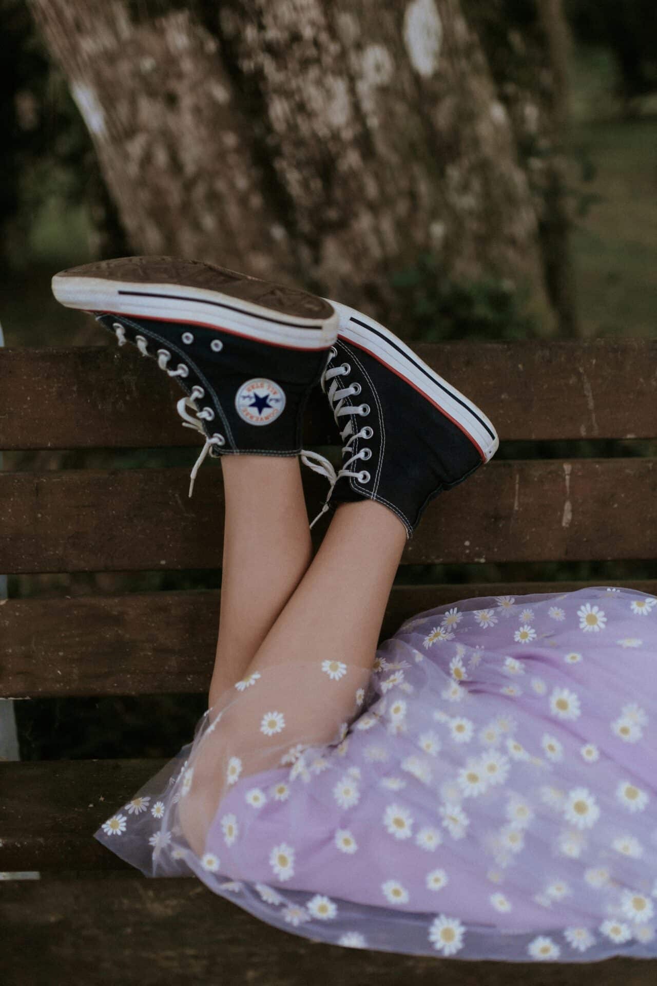 Buty na wiosnę – przegląd najmodniejszych modeli na nadchodzący sezon Nogi dziewczyny w czarnych trampkach Converse i fioletowej sukience w kwiatki