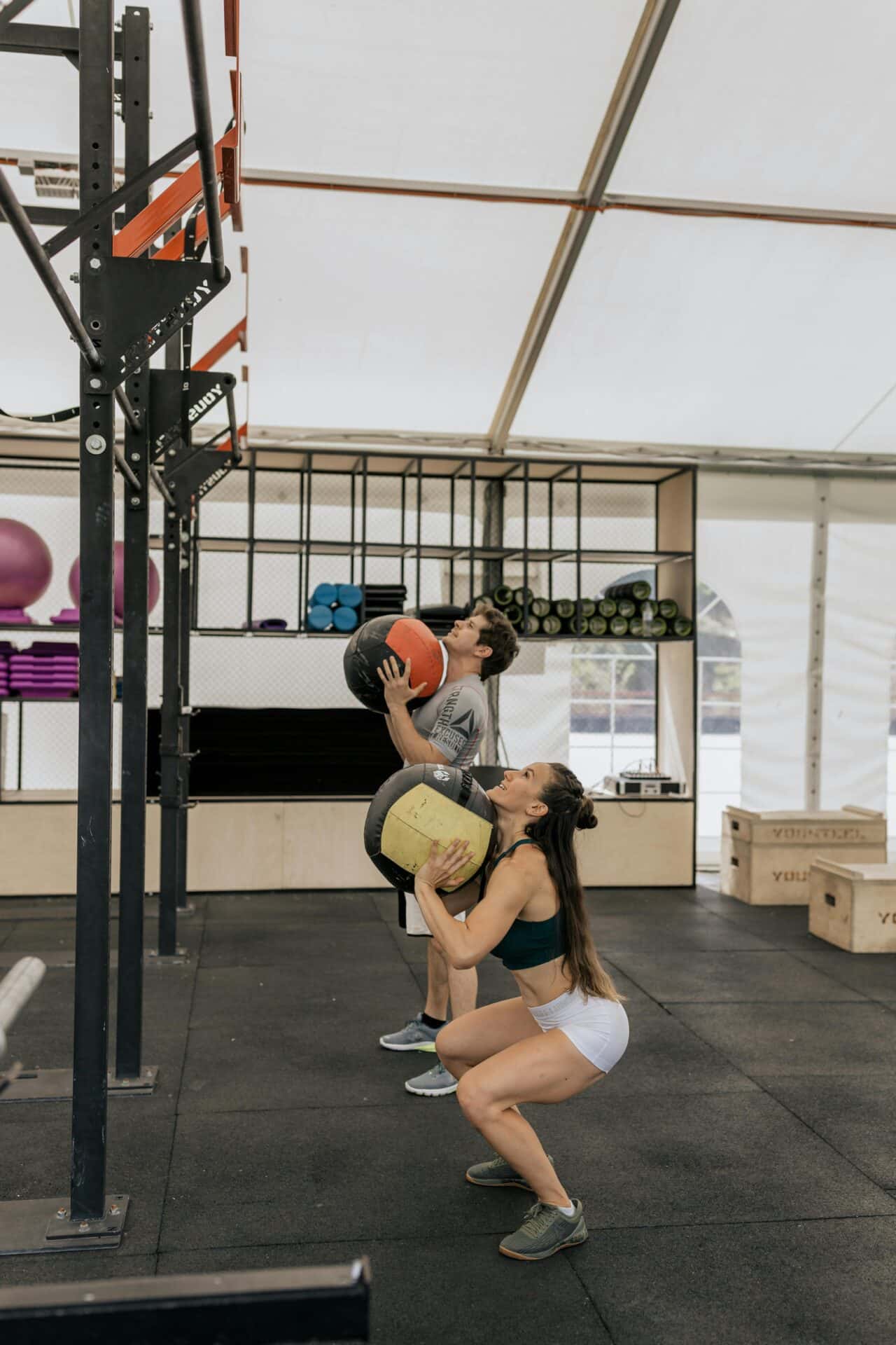 Kobieta i mężczyzna trenujący z piłkami lekarskimi pod konstrukcją crossfit