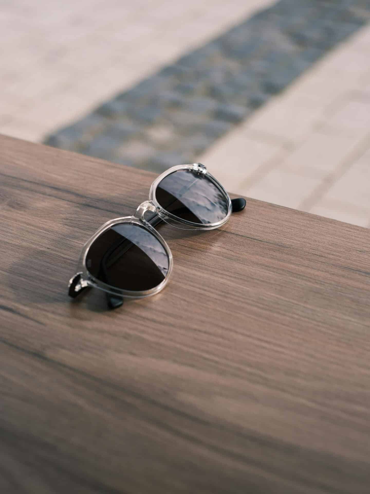 Okulary przeciwsłoneczne z filtrem UV – na co zwracać uwagę przy zakupie? Leżące okulary przeciwsłoneczne na drewnianym stole