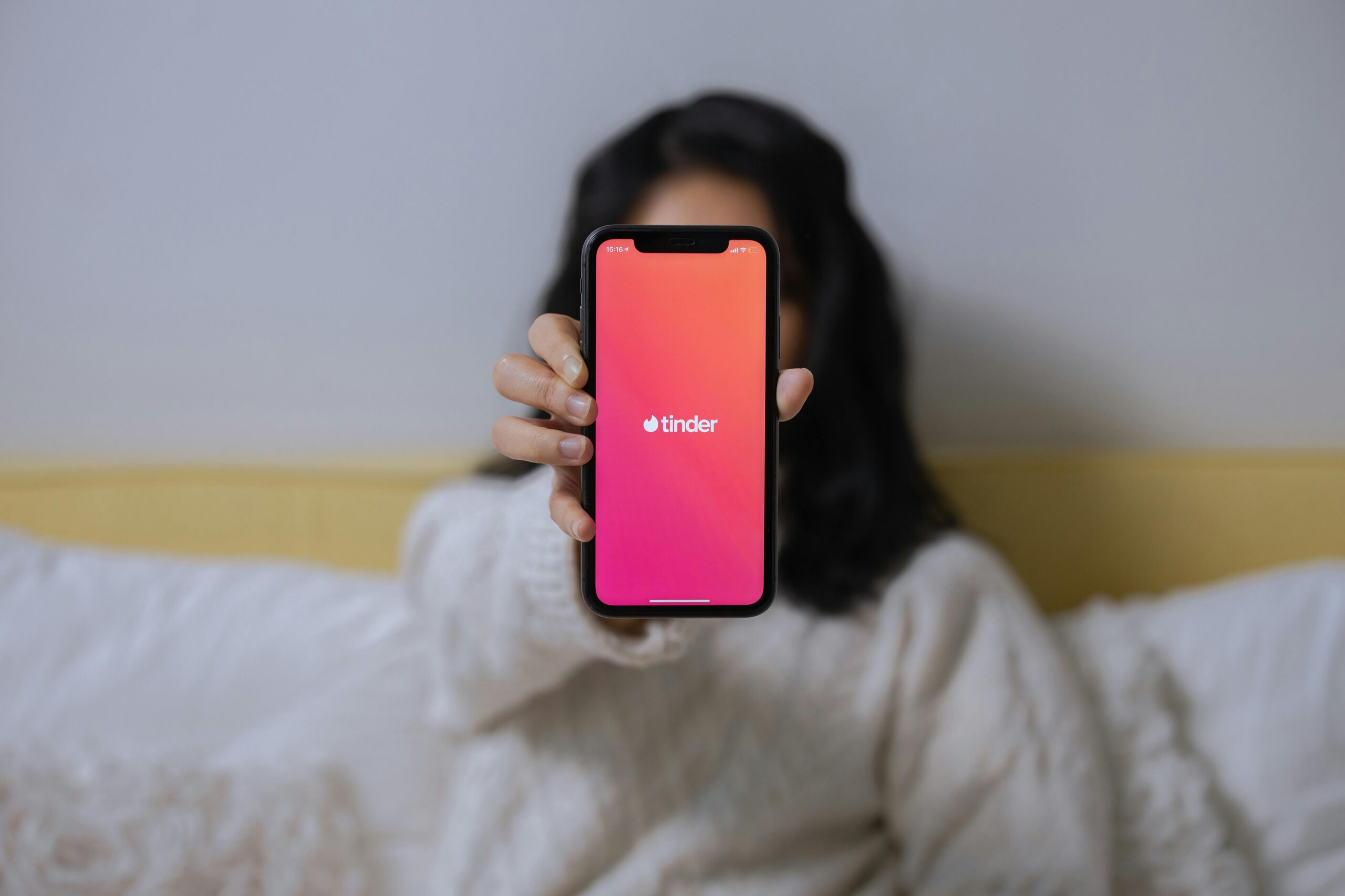 Kobieta w białym swetrze trzyma telefon z uruchomioną aplikacją Tinder
