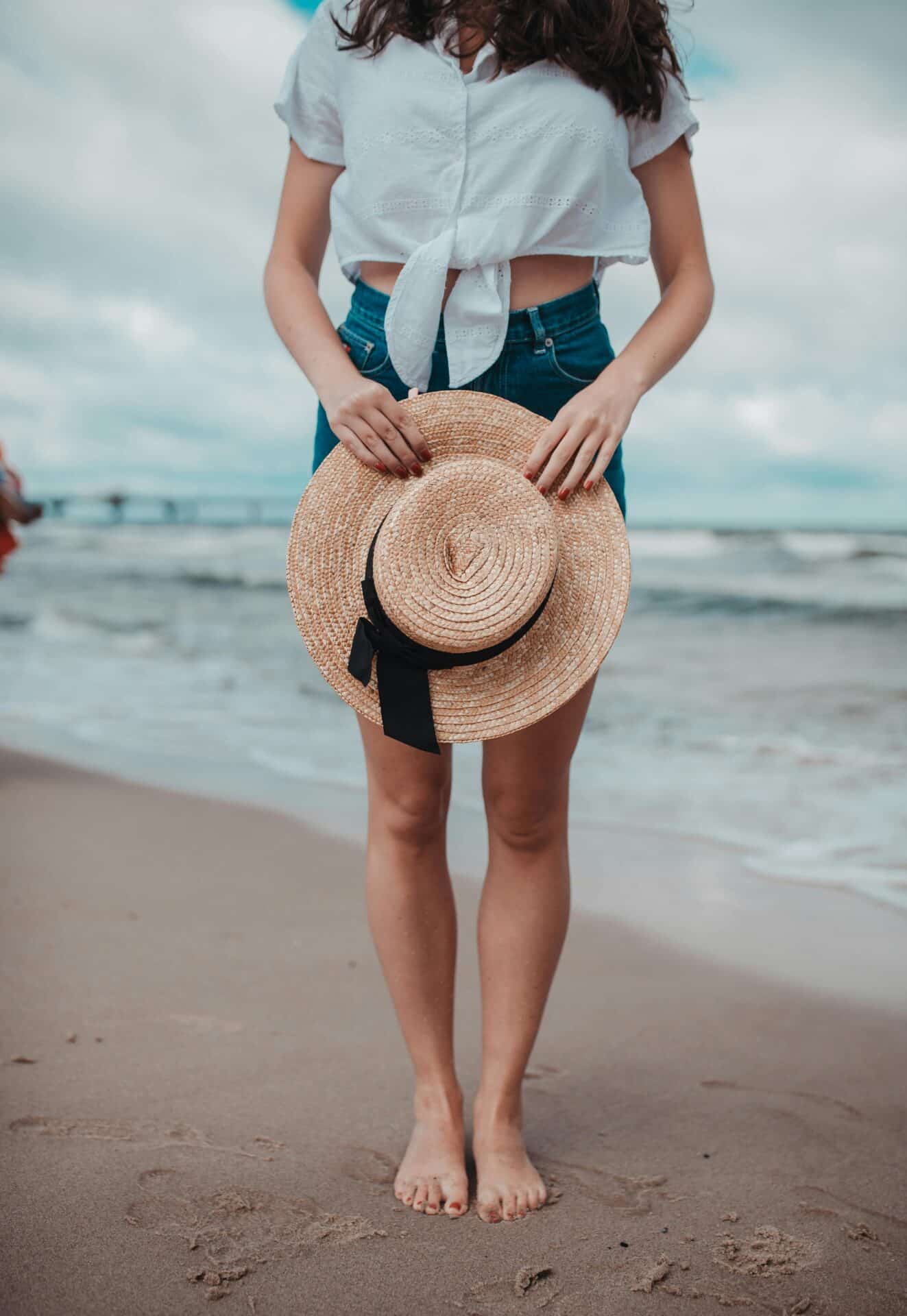 Kobieta w letnim stroju trzymająca słomkowy kapelusz na plaży