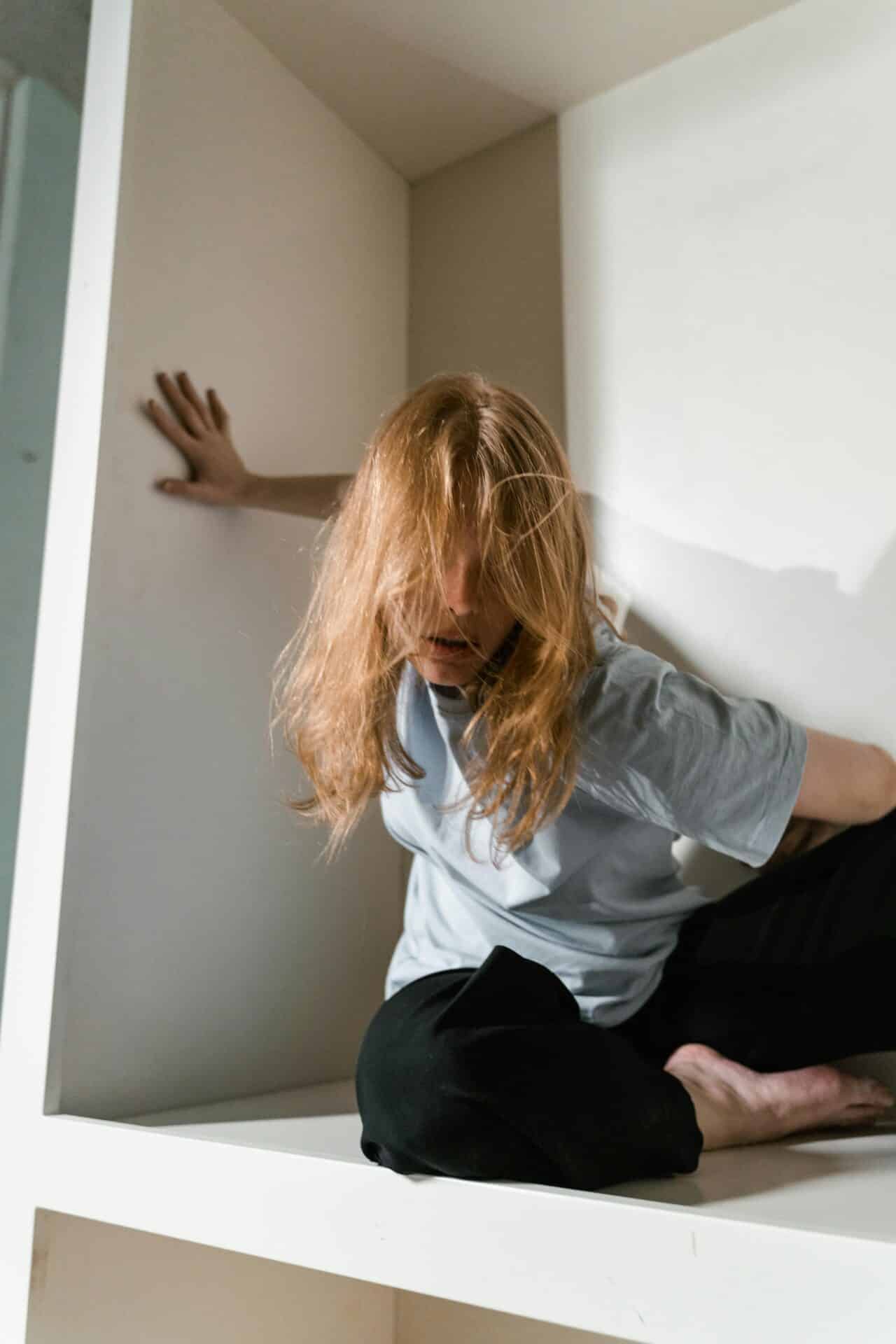 Kobieta z rozczochranymi włosami przy ścianie, wyrażająca niepokój