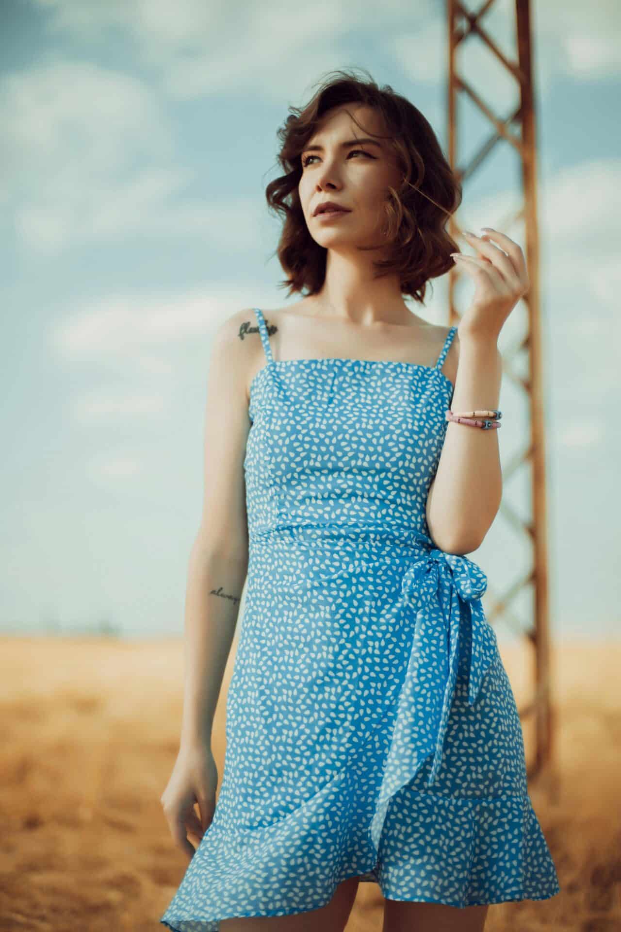 Młoda kobieta w błękitnej sukience w białe wzory na tle błękitnego nieba