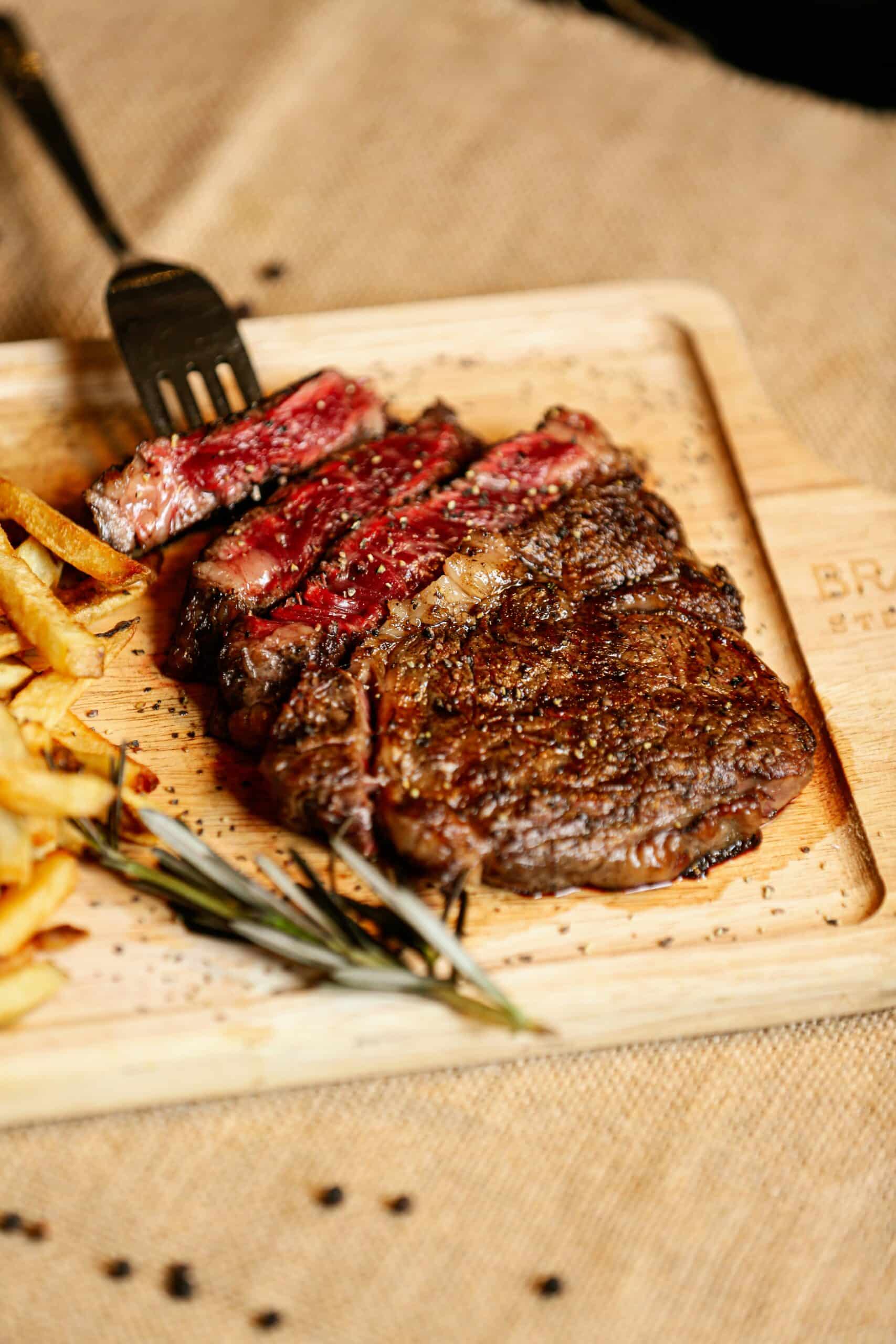 Pokrojony stek ribeye średnio wysmażony z frytkami i rozmarynem na drewnianej desce