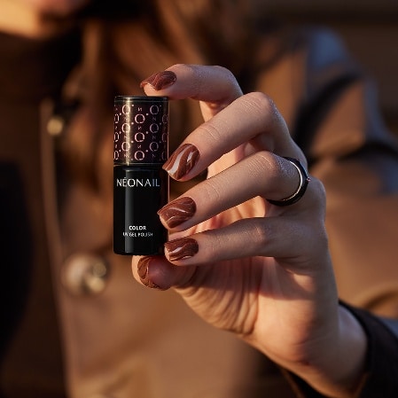 Dłoń z brązowym manicure trzymająca lakier hybrydowy NEONAIL