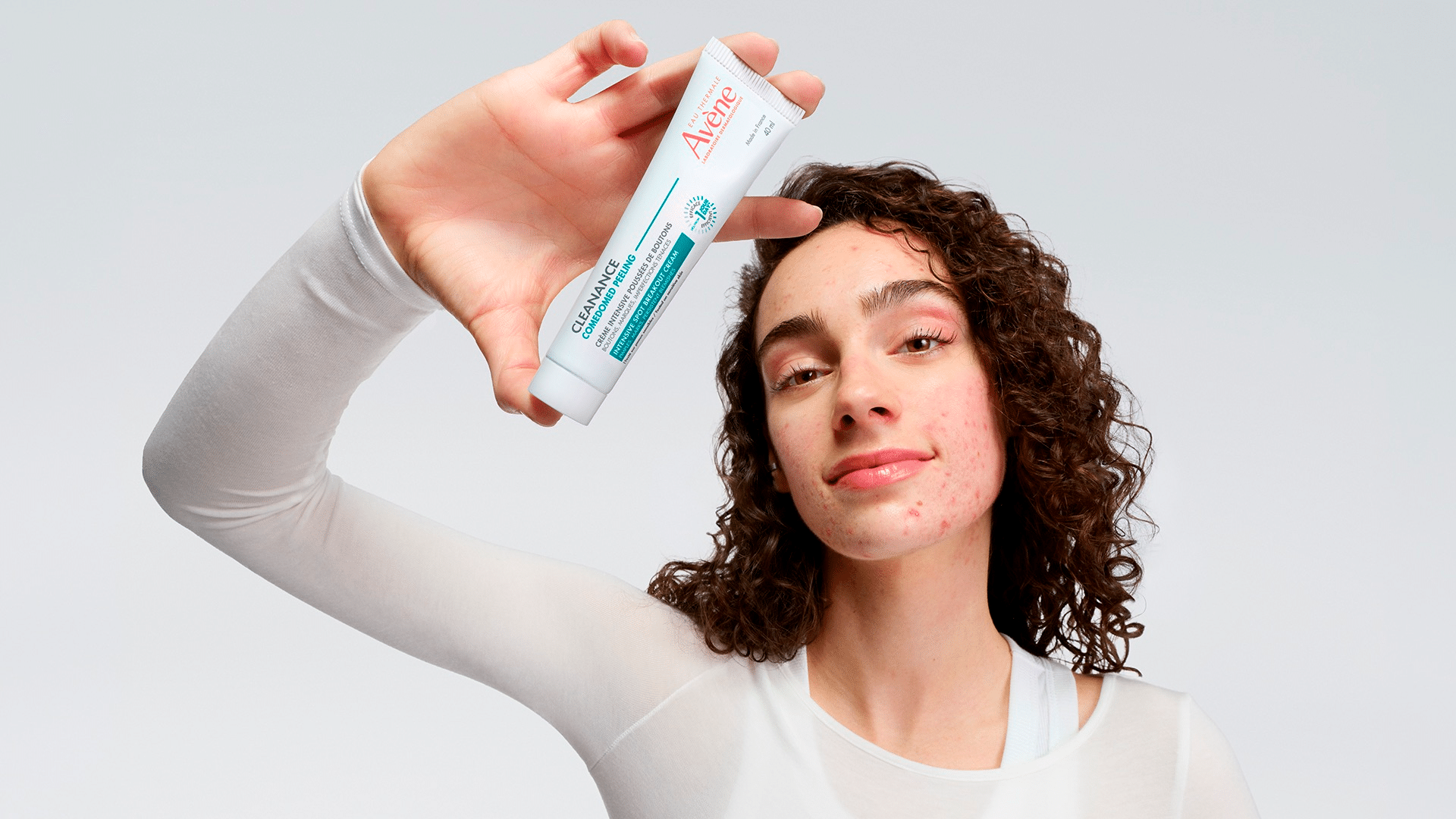 Osoba ze zmianami trądzikowymi trzyma krem Cleanance Comedomed Peeling marki Avène.